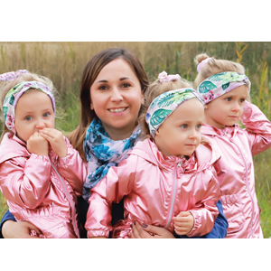 Natural Pharmaceuticals „OmegaMarine Junior+“ Motina apkabina tris mažas mergaites, apsirengusias identiškais rožiniais kombinezonais ir plaukų juostelėmis.a