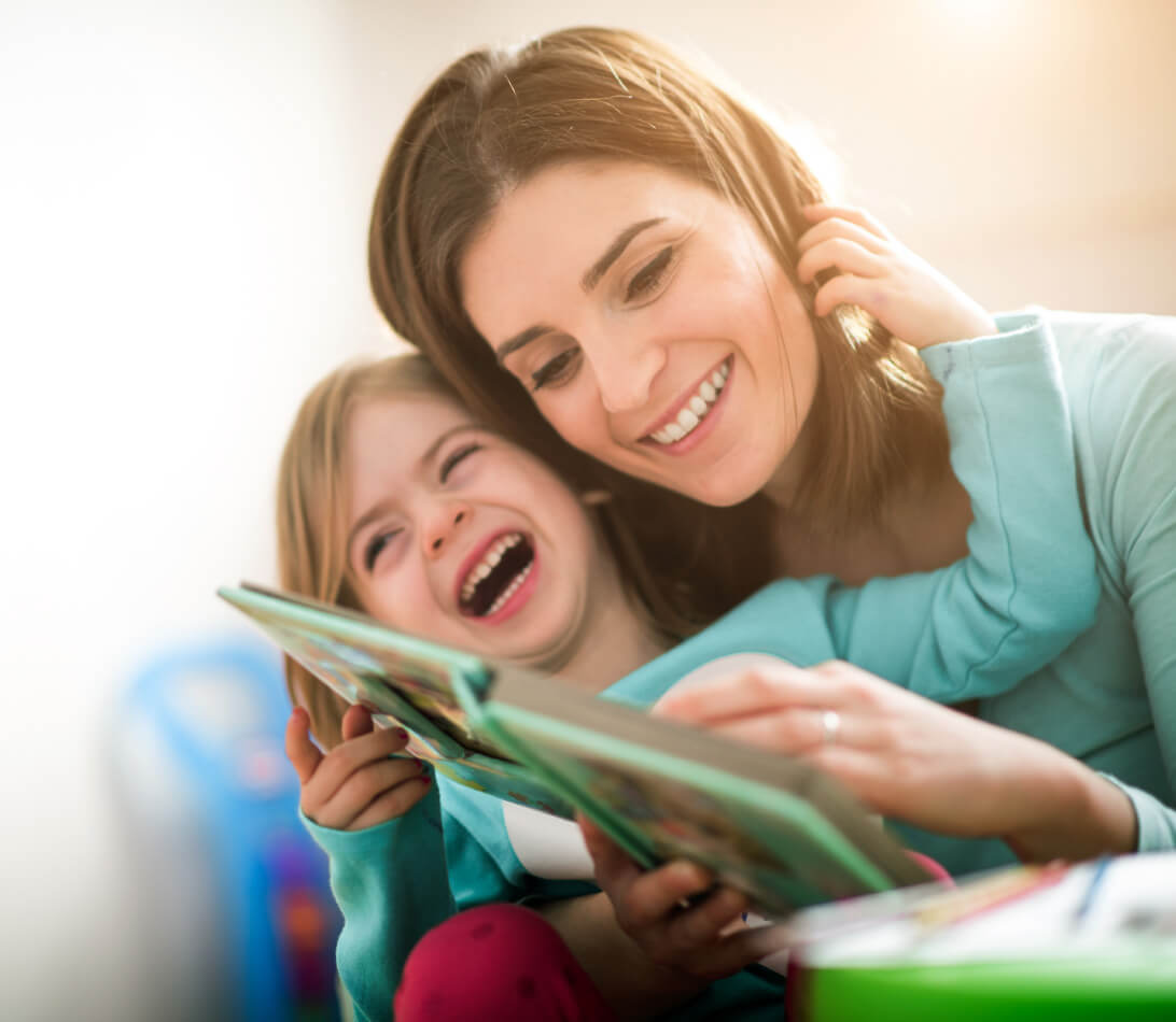 Natural Pharmaceuticals „OmegaMarine Junior+“ Motina ir dukra džiaugsmingai skaito paveikslėlių knygą kartu šviesiame kambaryje.